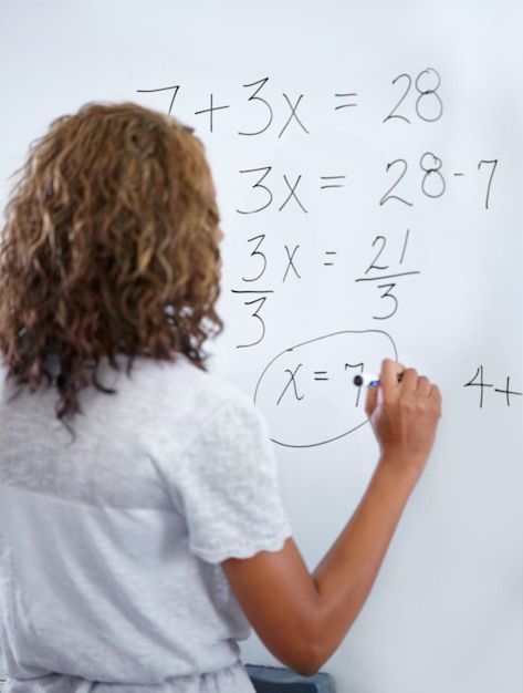 Foto maestra y escritura en pizarra para números o ecuaciones matemáticas en el aula vista trasera de una educadora o profesora con suma en la tabla para clase de aprendizaje o resolución de problemas