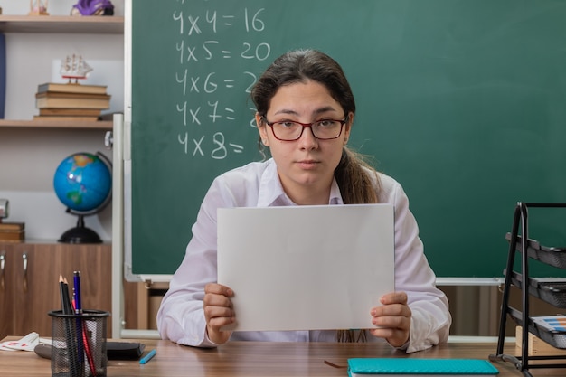 maestra joven con gafas sosteniendo páginas en blanco