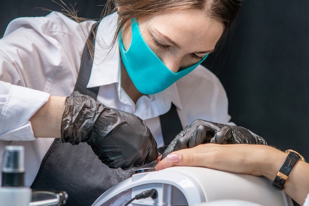 La maestra de manicura femenina hace una manicura de hardware en guantes negros quitando el viejo recubrimiento de esmalte de gel en el salón