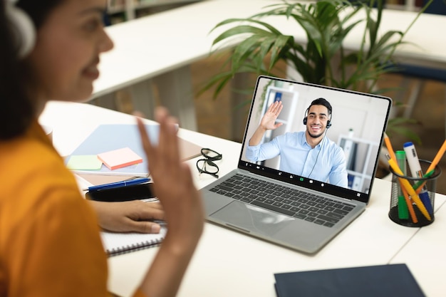 Maestra negra agitando la mano en la pantalla de videollamada de la computadora portátil