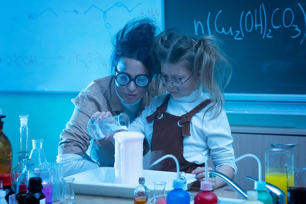 Maestra y niña durante la lección de química mezclando productos químicos en un laboratorio