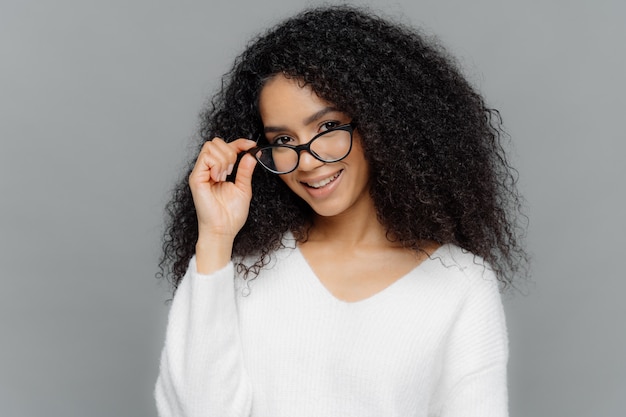 Maestra satisfecha mantiene la mano en el marco de las gafas, sonríe feliz