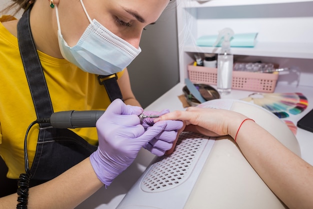 Una maestra usa un cortaúñas eléctrico para quitar el esmalte de uñas durante una manicura en el salón.