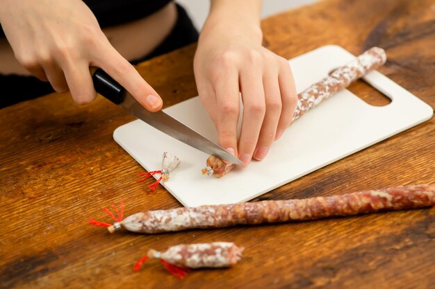 Maestría culinaria Las manos femeninas cortan hábilmente salchichas en una tabla de cortar mostrando habilidades de cocina y el arte de la preparación de alimentos