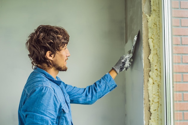 El maestro está aplicando masilla blanca en una pared y manchando con una  espátula en una sala de renovación de la casa durante el día