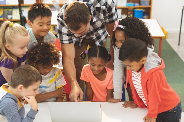 Maestro aprendiendo en sus niños de la escuela cómo usar una computadora portátil en el aula en la escuela