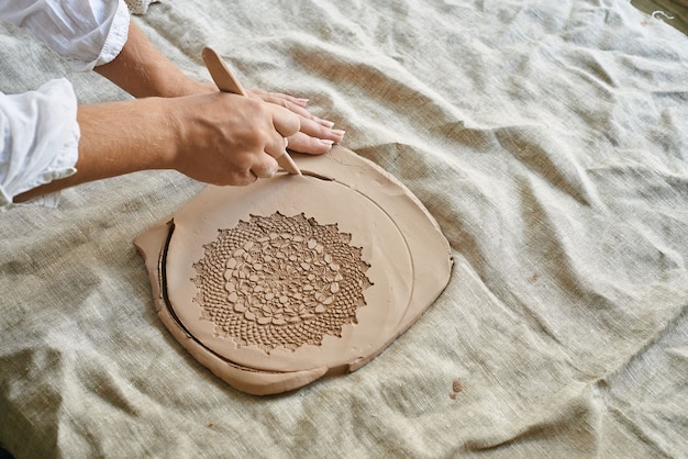 Foto el maestro artesano rueda la arcilla sobre la mesa, transfiere el patrón de la servilleta a la masa de arcilla.