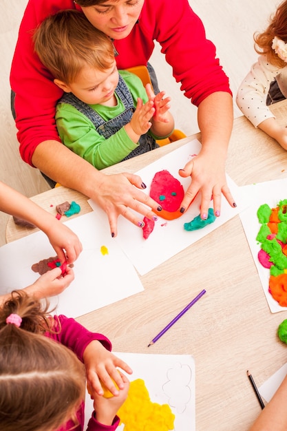 El maestro ayuda al niño a hacer una figura de plastilina sobre la mesa.