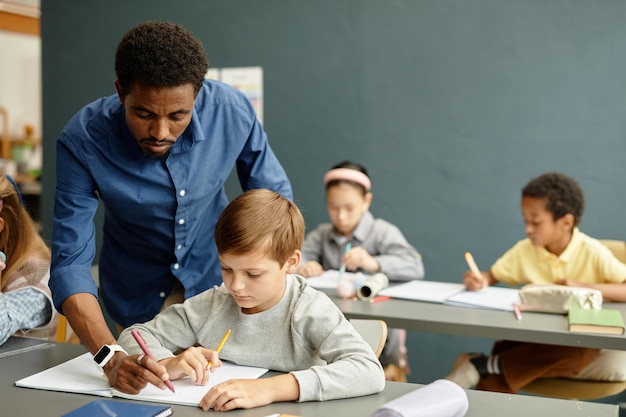 Un maestro ayuda a un niño con la ortografía mientras escribe en un cuaderno en la escuela
