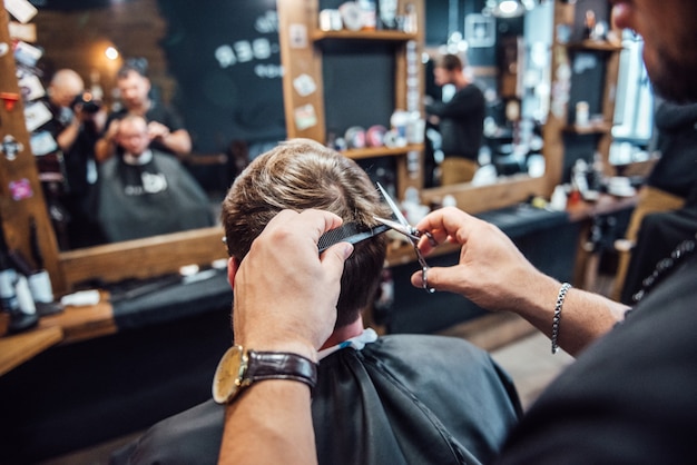 El maestro de la barbería afeita y corta al hombre frente al espejo