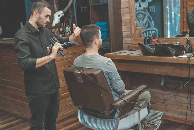 El maestro de Barbeshop le sopla el cabello y la barba al cliente con un secador de pelo. Lavado de cabello y barbas. Peluquero para hombres.