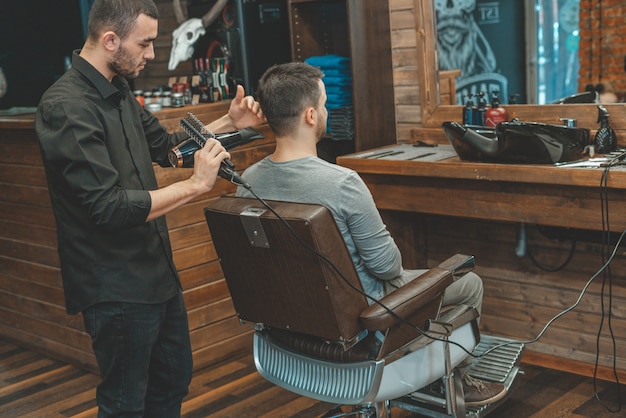 El maestro de Barbeshop le sopla el cabello y la barba al cliente con un secador de pelo. Lavado de cabello y barbas. Peluquero para hombres.