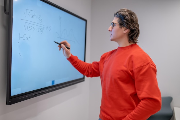 Un maestro con camisa roja escribiendo en la pizarra en la lección