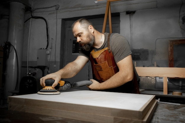 Maestro carpintero brutal muele los espacios en blanco de madera con la máquina en el taller