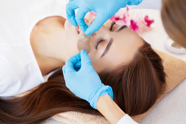 Maestro y cliente en un salón de belleza, parches para el cuidado de la piel debajo de los ojos.