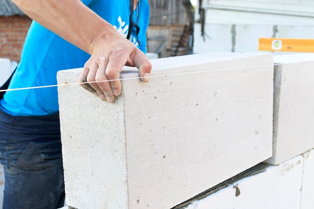 El maestro coloca un muro de bloques El constructor construye un muro de hormigón hecho de bloques de cemento en el sitio de construcción de un edificio residencial con sus propias manos Concepto de construcción de una casa