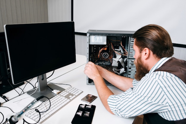 Maestro de computadora que desmonta la CPU con herramientas especiales. Lugar de trabajo de reparador con juego de tornillos y monitor en la mesa. Concepto de renovación de PC