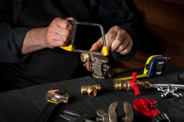 Un maestro corta accesorios de latón con una sierra antes de reparar o conectar un gasoducto.