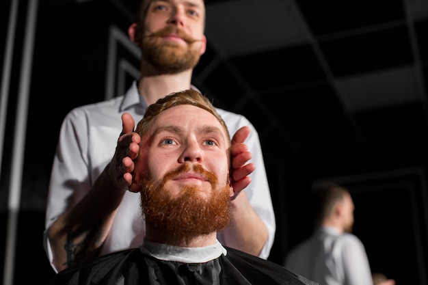 El maestro corta el cabello y la barba en la peluquería. Peluquero hace peinado con tijeras y un peine de metal. Un cliente satisfecho.