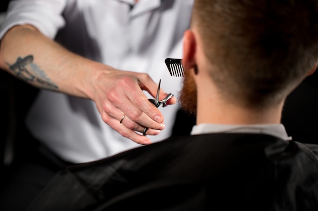 El maestro corta el cabello y la barba en la peluquería. Peluquero hace peinado con tijeras y peine de metal.