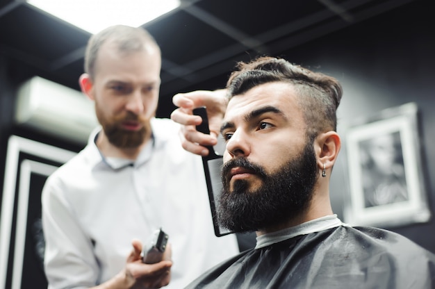 Maestro corta el pelo y la barba de los hombres en la barbería, el peluquero hace el peinado para un hombre joven.