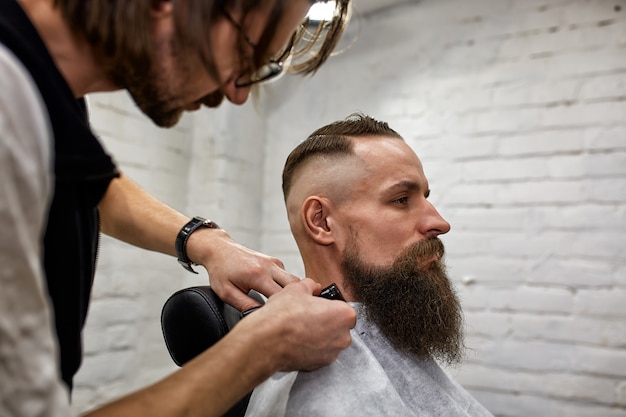 Maestro corta el pelo y la barba de los hombres en la barbería