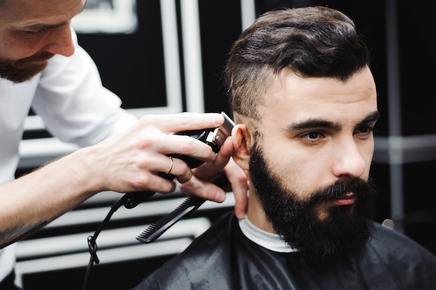 Maestro corta el pelo y la barba de los hombres en la peluquería, peluquería