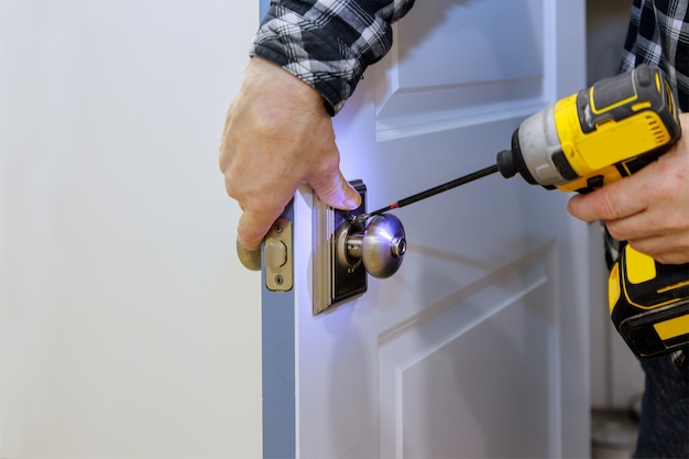 Maestro con destornillador instala acceso a la puerta de la habitación nueva cerradura en casa.