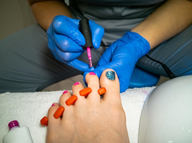 Maestro enguantado hace una pedicura para un cliente closeup sin rostro mujer en un salón de uñas pinta sus uñas