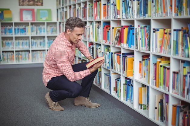 Maestro de escuela atento seleccionando el libro en la biblioteca