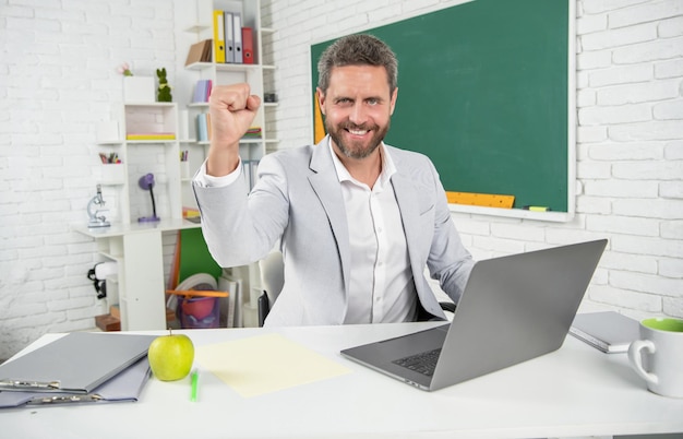 Maestro de escuela exitoso en el aula con computadora en la pizarra