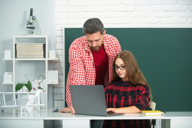 Maestro de escuela primaria y alumno haciendo la tarea usando una computadora portátil en el aula