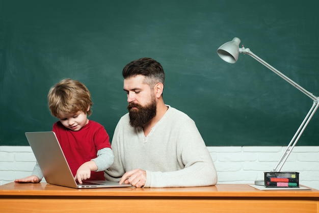 Maestro de escuela primaria y estudiante en el aula maestro y colegial usando una computadora portátil en la clase de tiza