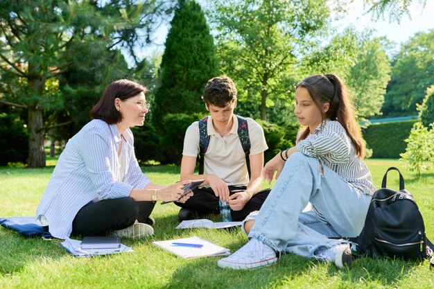 Maestro de escuela psicólogo trabajador social hablando con adolescentes sentados en el césped