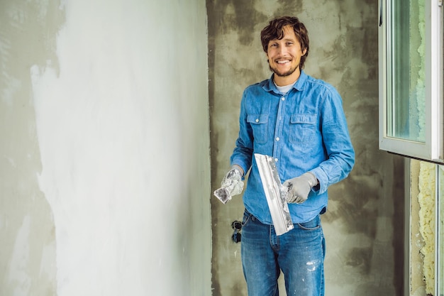 El maestro está aplicando masilla blanca en una pared y manchando con una espátula en una sala de renovación de la casa durante el día