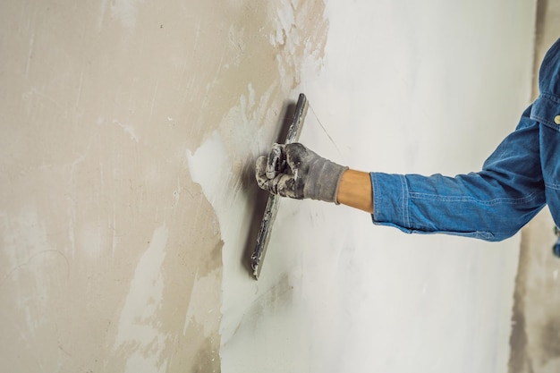 El maestro está aplicando masilla blanca en una pared y manchando con una espátula en una sala de renovación de la casa durante el día