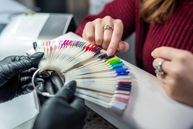 Un maestro de extensión de uñas profesional selecciona el color para su cliente durante el concepto de manicura epidémica