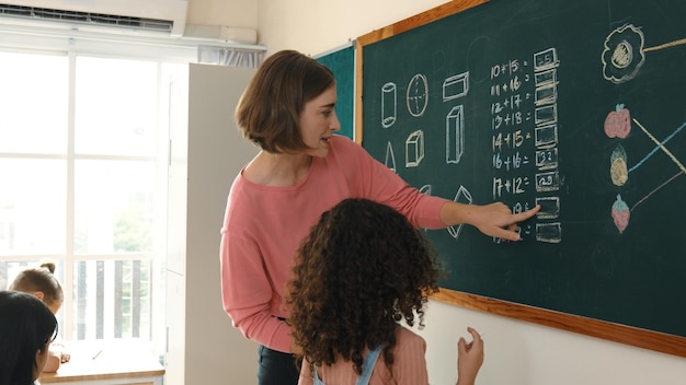 Un maestro hábil mirando a una niña africana escribiendo una respuesta en la pizarra Pedagogía