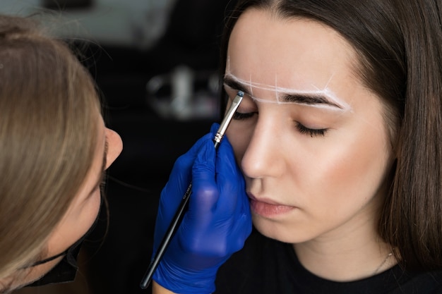 El maestro hace el procedimiento de corrección de cejas para una niña.