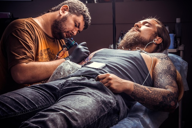 Maestro haciendo tatuajes en el estudio de tatuajes./El tatuador profesional hace fotos de tatuajes en el estudio de tatuajes.