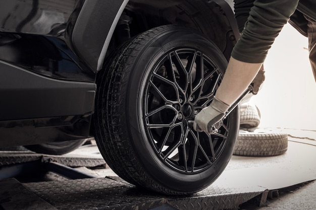 Un maestro instalador de neumáticos atornilla una nueva rueda negra a un automóvil en un primer plano del servicio de neumáticos