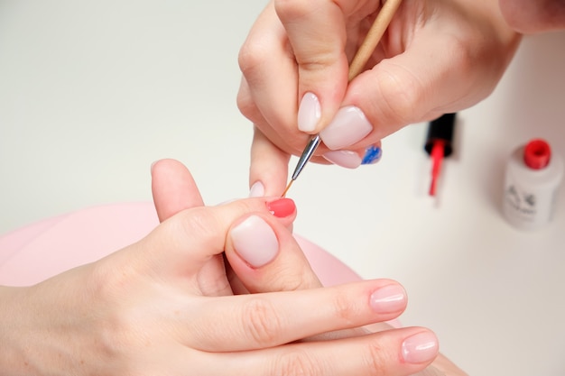 Foto el maestro de manicura aplica un esmalte de uñas brillante a las uñas del cliente en un salón de belleza.