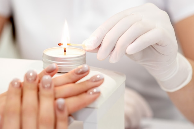 Maestro de manicura en guantes blancos encendiendo velas con fósforo en salón de uñas