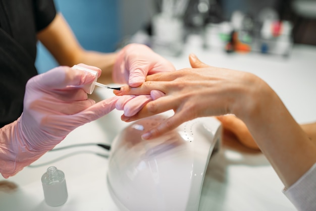 Foto maestro de manicura en guantes rosa aplicando esmalte de uñas a clienta