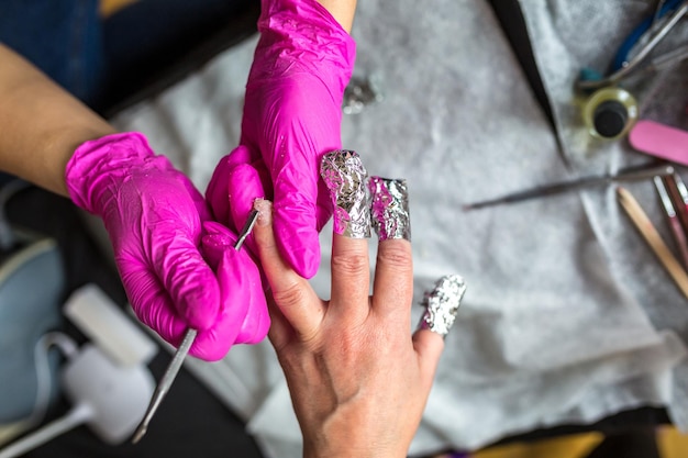 Maestro de manicura en guantes rosas raspando la vieja capa de barniz en salón de manicura usando taladro Manicura profesional en clínica de cosmetología Higiene para pies en salón de belleza