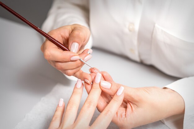 Maestro de manicura manicura francesa dibujo barniz blanco en la punta de la uña con un pincel fino de cerca