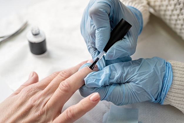 Maestro de manicura en máscara y guantes poniendo esmalte de gel en las uñas de un cliente