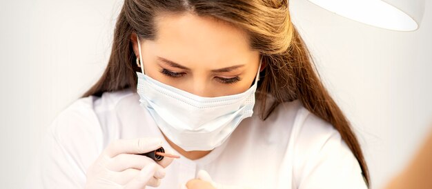 Foto maestro de manicura en la máscara protectora blanca está pintando uñas con esmalte de uñas en un salón de uñas