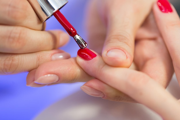 Maestro manicurista hace manicura roja en la mano de la mujer joven