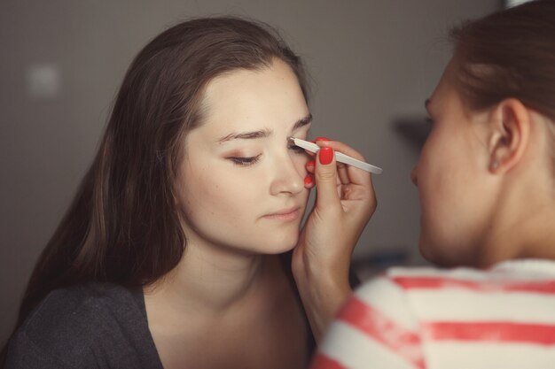 El maestro de maquillaje modela la forma de las cejas en el rostro de una chica joven y hermosa.